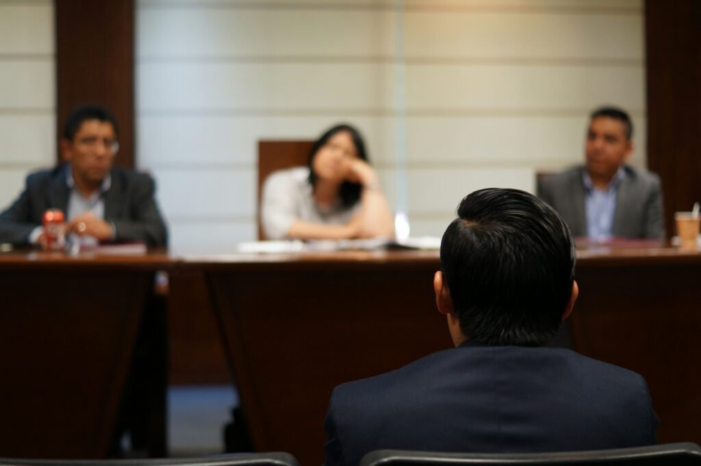 A man in a suit facing the background, looking at a panel of people during a testimony in a court of law.